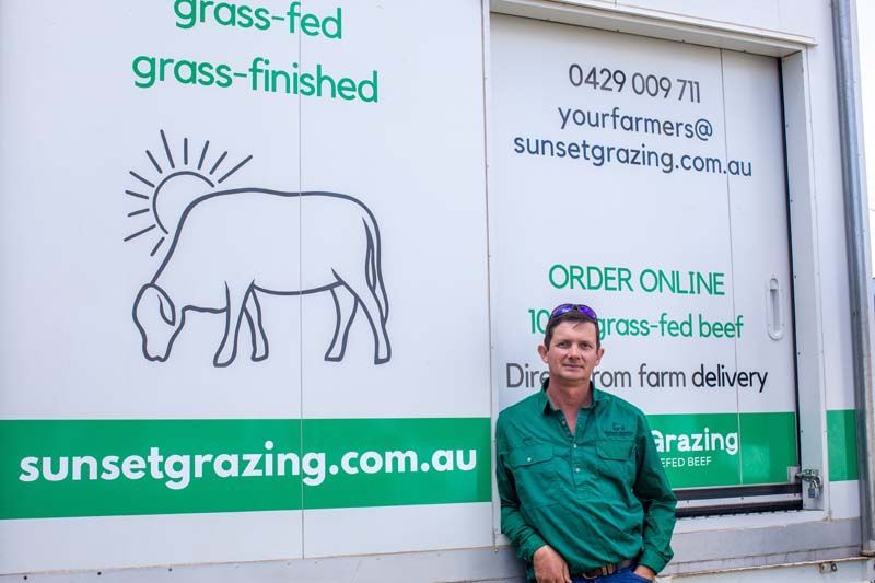 Man standing beside a white delivery truck with green “sunsetz grazing” branding and a cow logo
