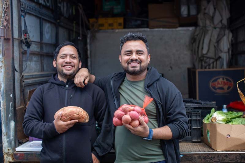 Two smiling people holding bread and produce in a market stall