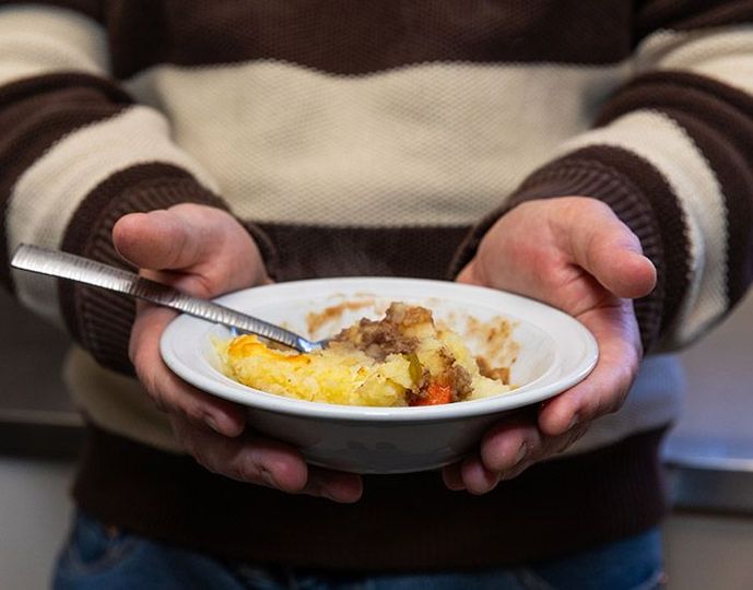 Hands holding a bowl of food with a spoon, including eggs and browned toppings.