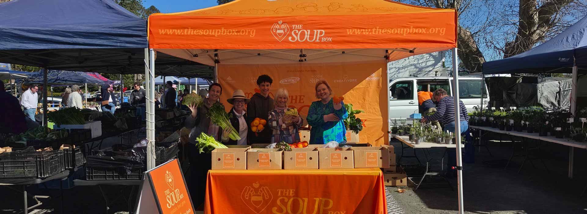 Orange outdoor booth with people behind a table at a market or event