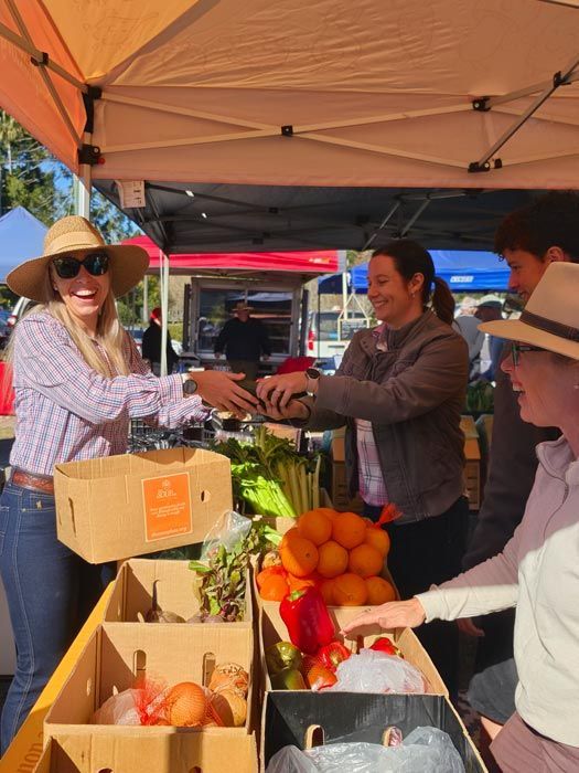 Three smiling people posing at a Food & Ag Network booth under an orange tent.