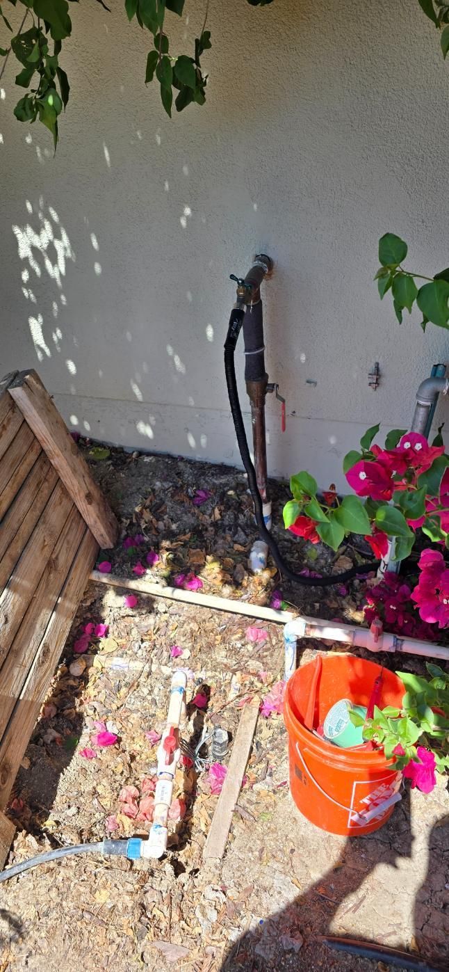 Small patio garden with potted flowers, a wooden planter, and an orange bucket against a stucco wall.