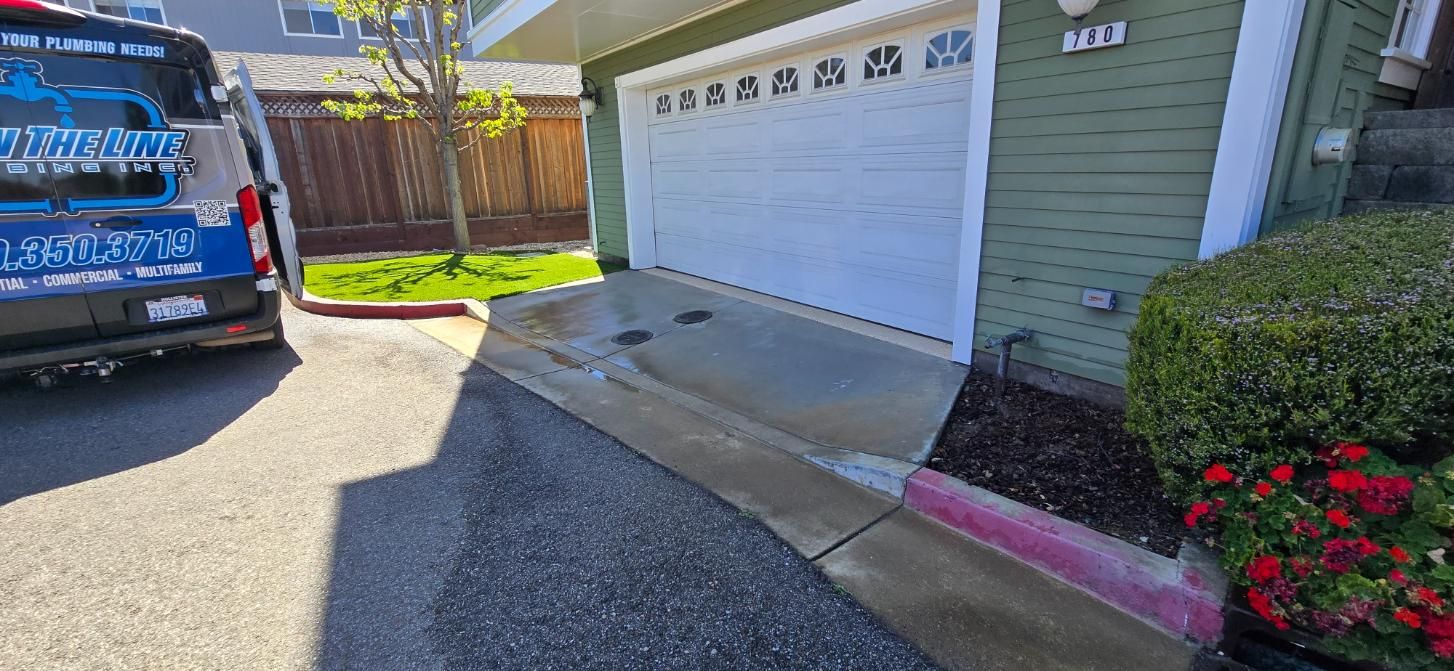Driveway beside a white garage door, with a blue work van parked on the left and sunlight on the concrete.
