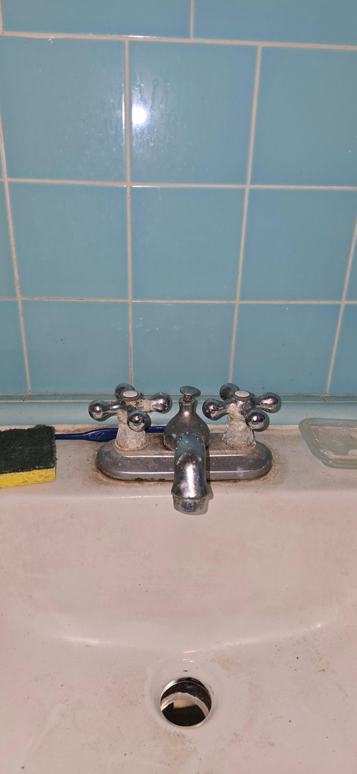 Bathroom sink with chrome faucet and blue tiled wall behind it.