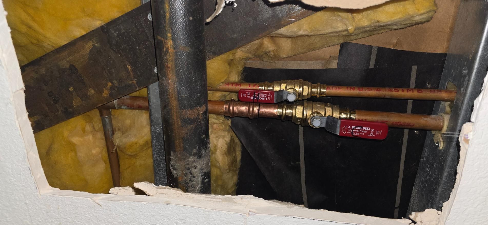 Exposed plumbing pipes with red valves inside a wall opening, surrounded by insulation.