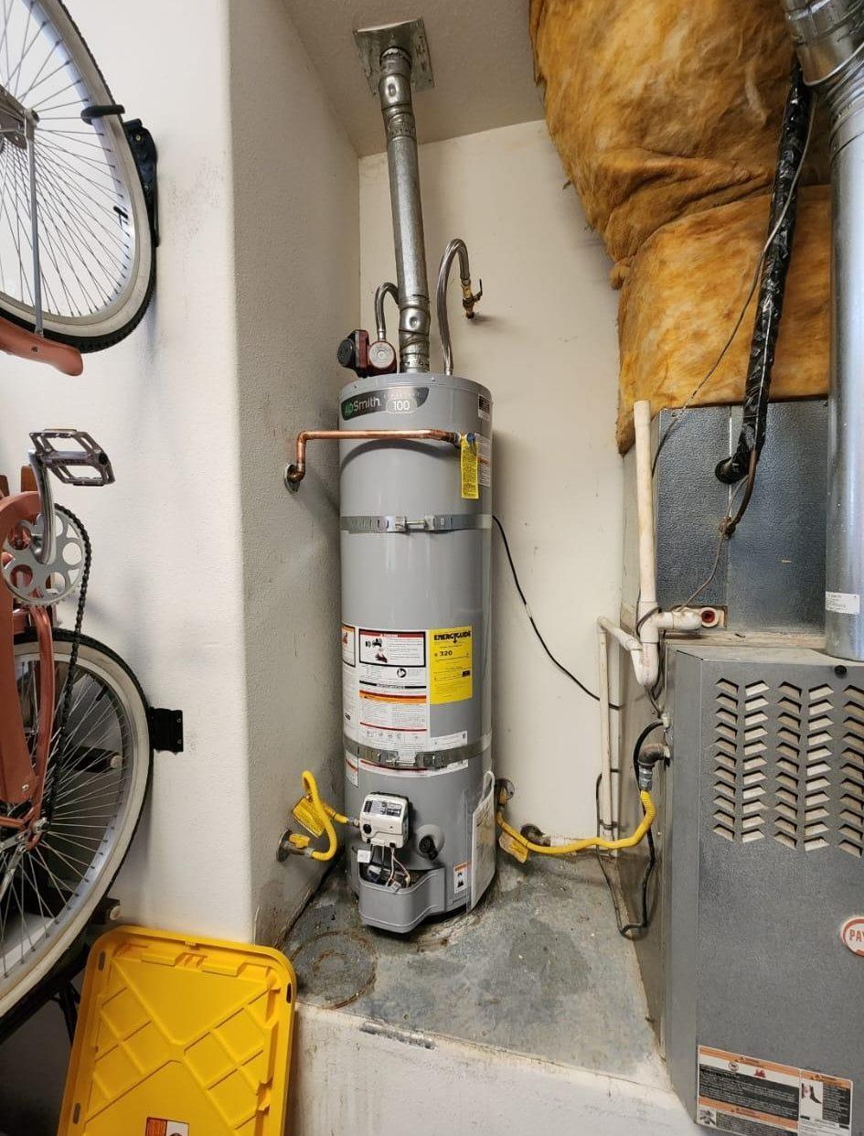 Water heater and furnace in a small utility closet with exposed pipes and yellow insulation.