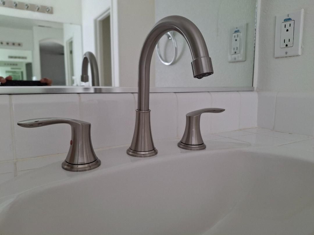 White bathroom sink with brushed nickel faucet and handles, seen in a mirror reflection