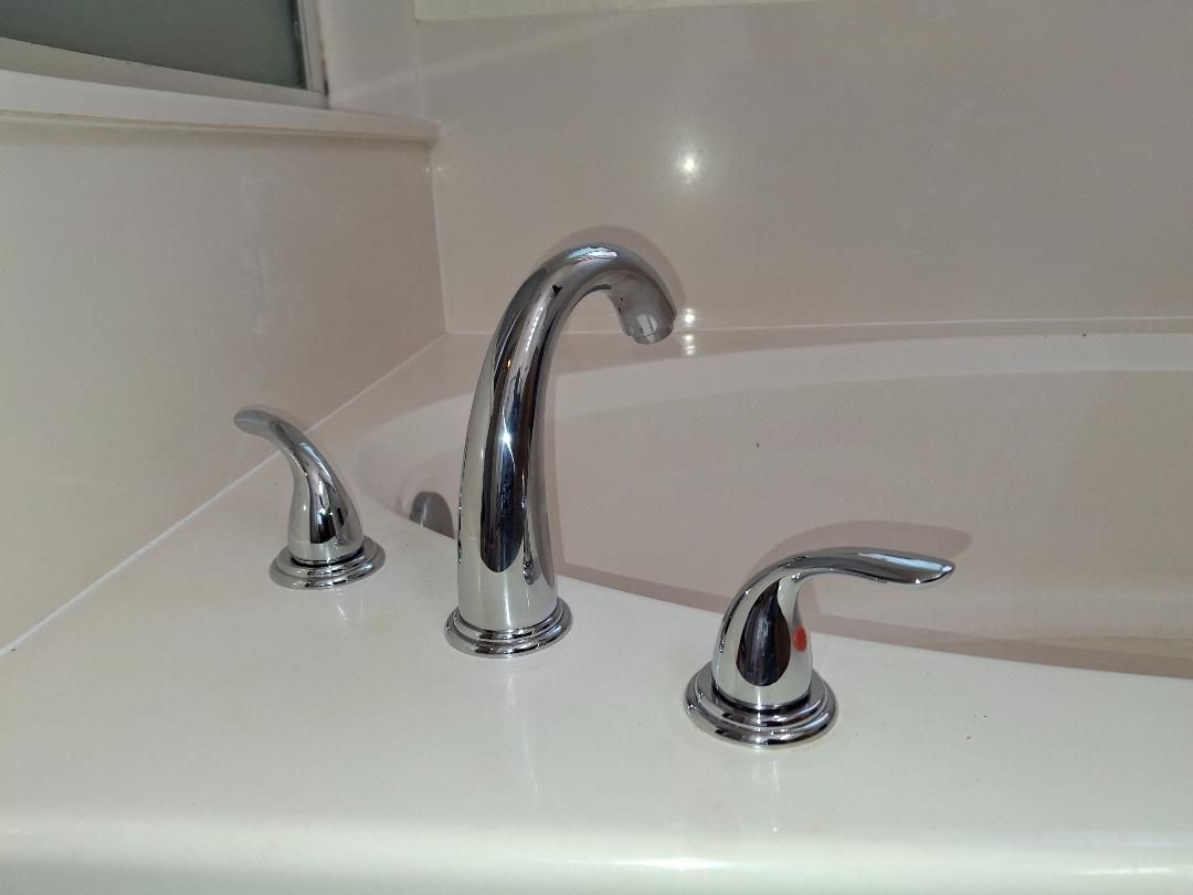 Chrome bathtub faucet and two handles on a white tub ledge
