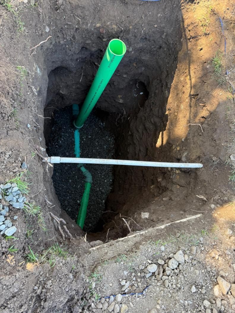 Open hole in dirt with green PVC pipes and a white rod crossing the shaft