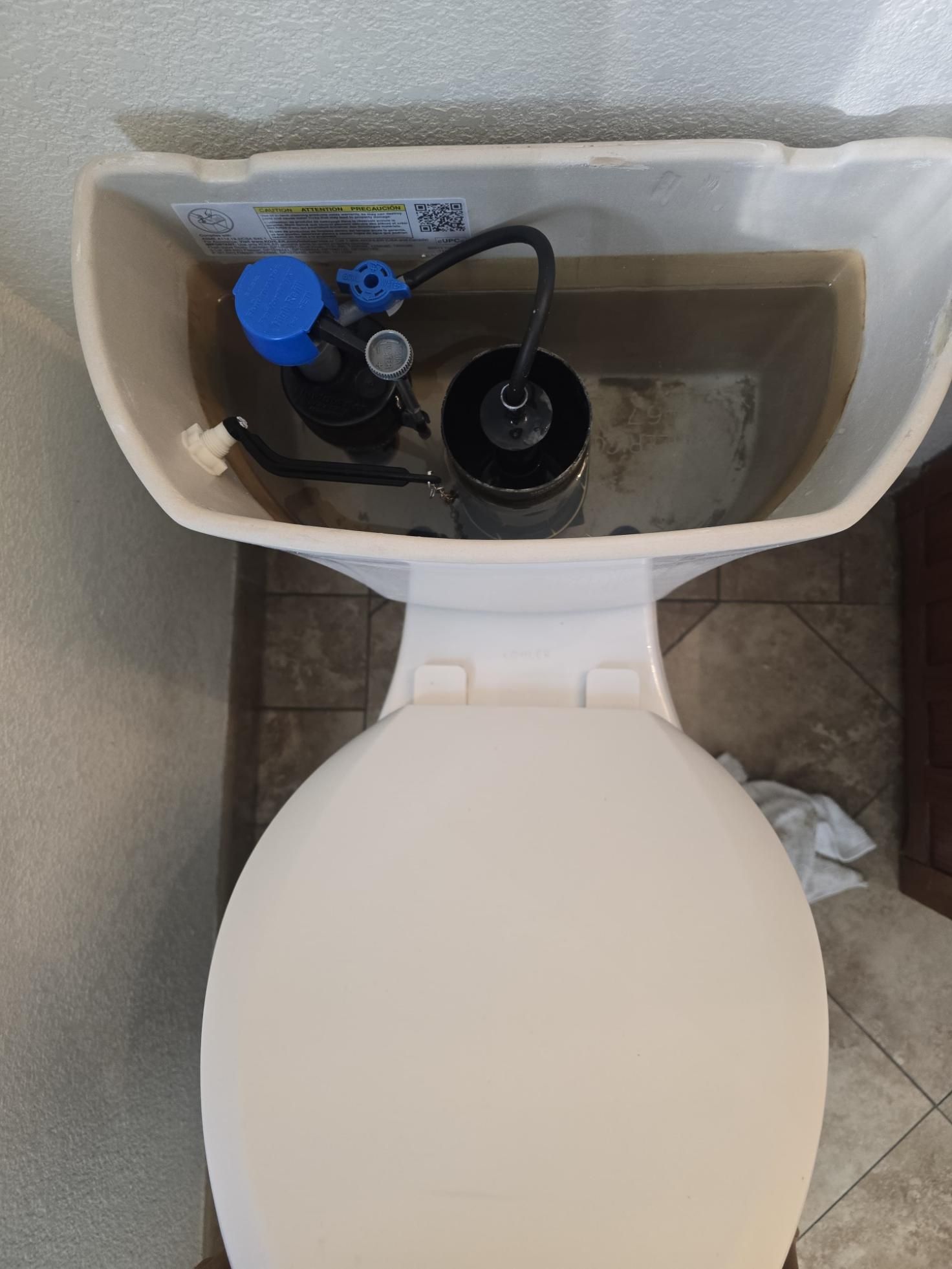 Open toilet tank with blue and black flush components above a white toilet seat