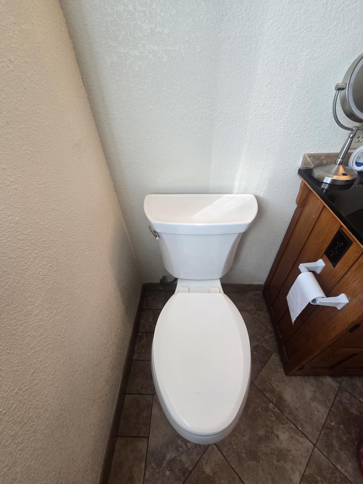 Small bathroom with a white toilet beside a wooden cabinet and tiled floor.