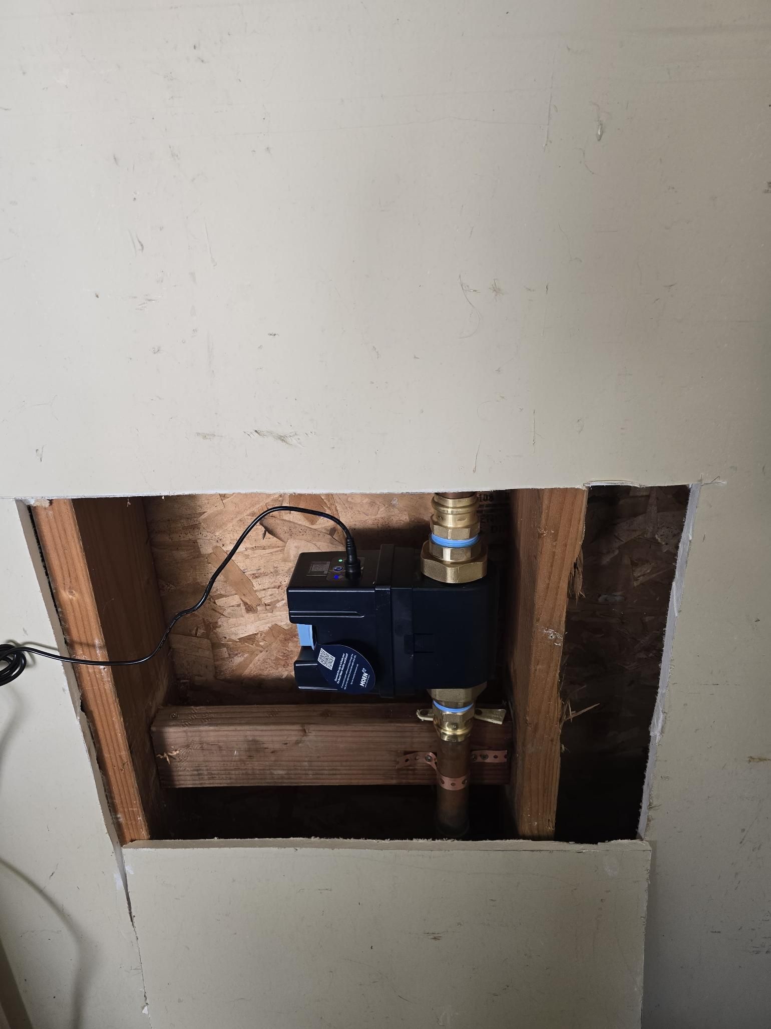 Wall opening showing a water valve and copper pipes inside a wall cavity