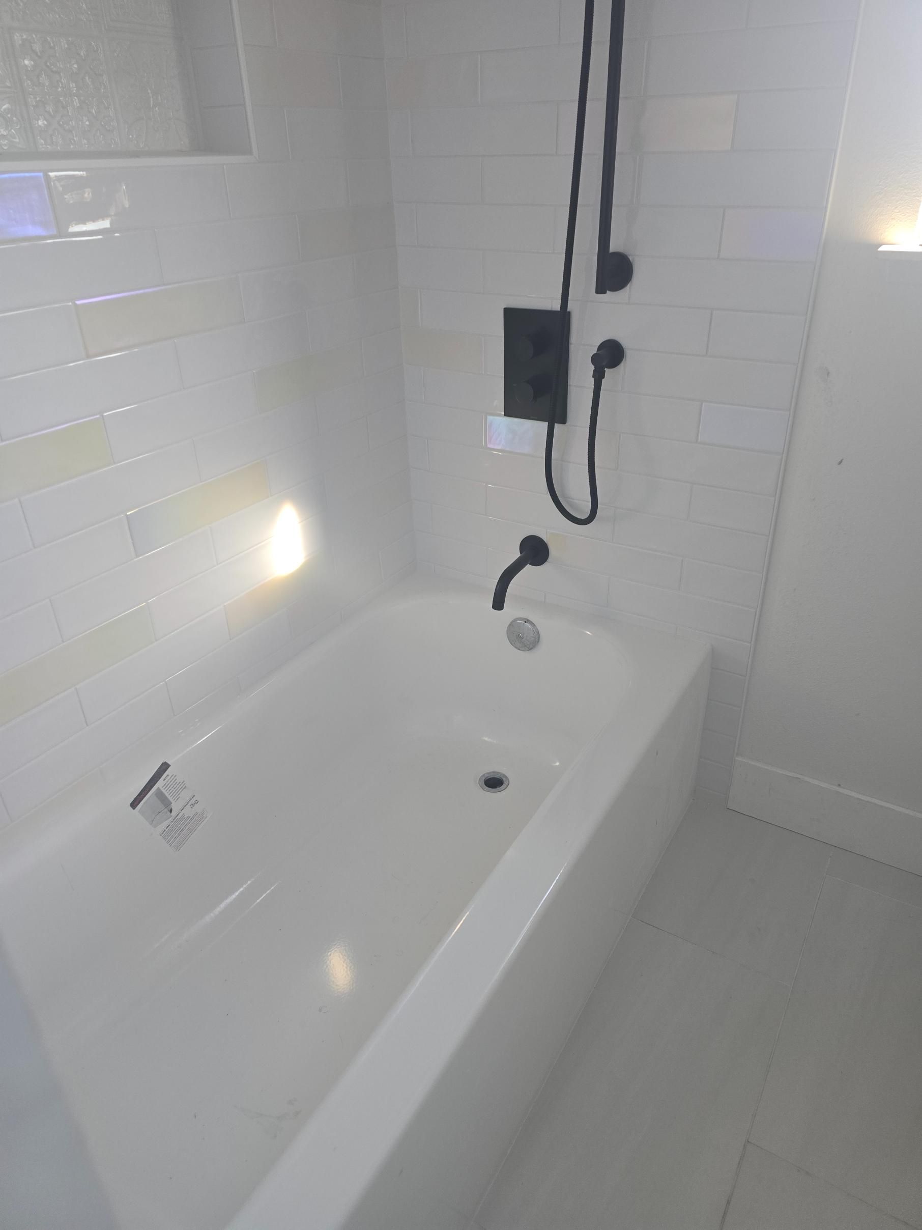 Accessible white bathroom with a bathtub, showerhead, grab bars, and tiled walls