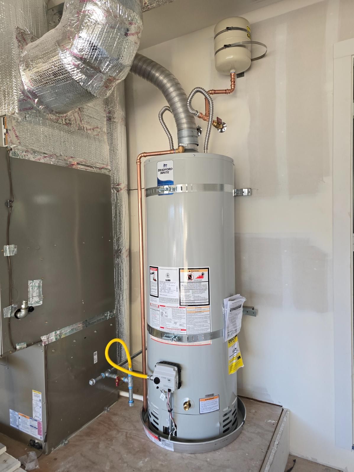 Water heater in a utility closet with connected venting, pipes, and a furnace beside it.