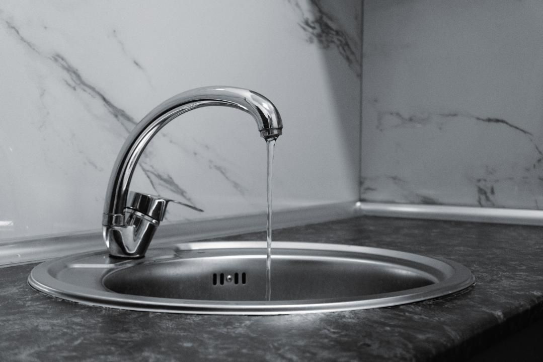 Chrome faucet running into a stainless steel sink on a marble countertop.