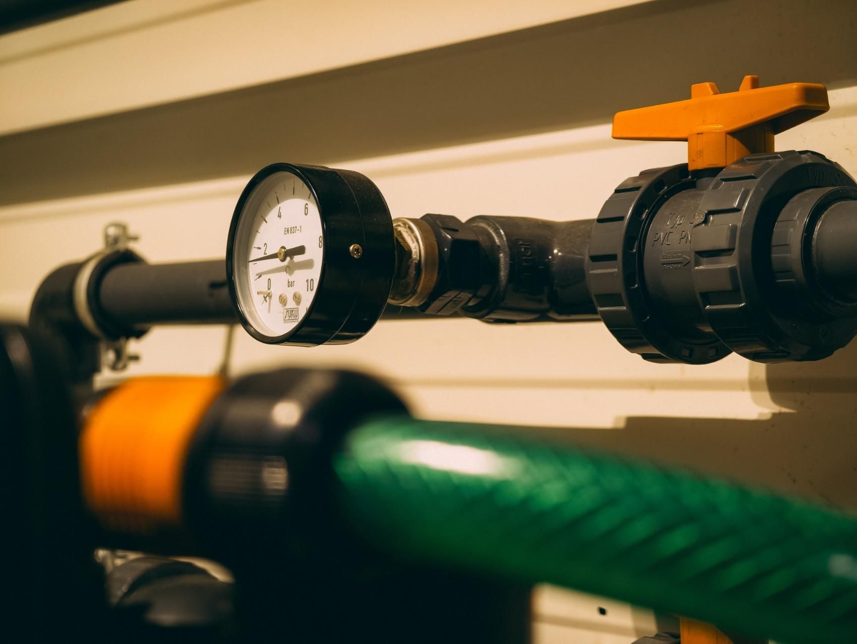 Pressure gauge and pipe valves with a green hose in an industrial setting