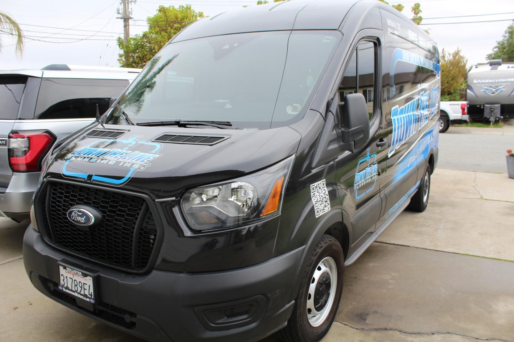 Black Ford transit van with blue graphics parked in a lot on a wet day