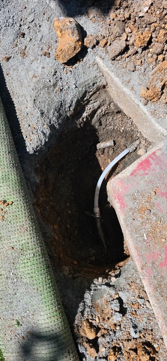 Close-up of a muddy trench with a metal pipe and broken concrete or stone debris.