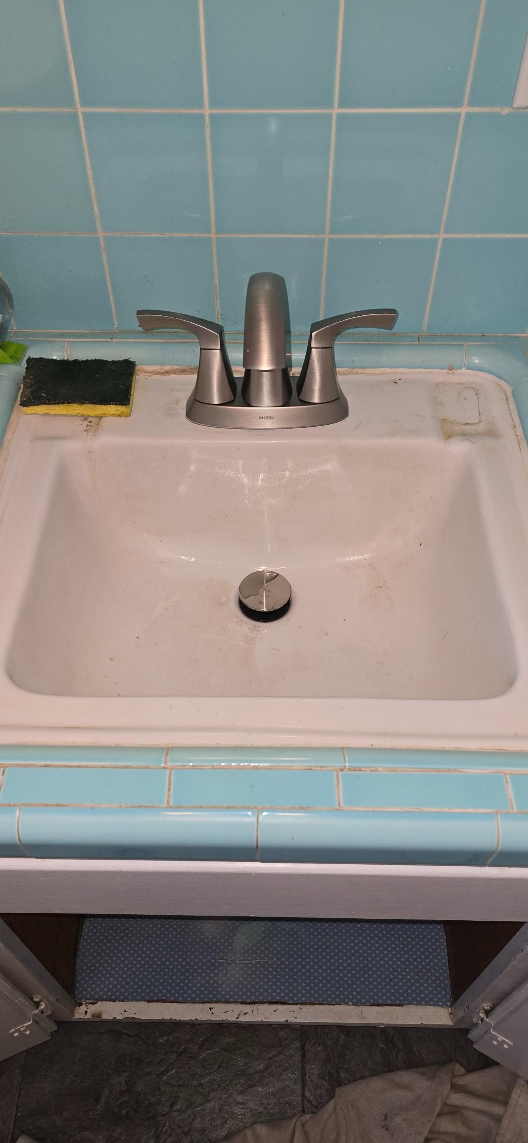 White bathroom sink with silver faucet against blue tile wall and an exposed pipe below
