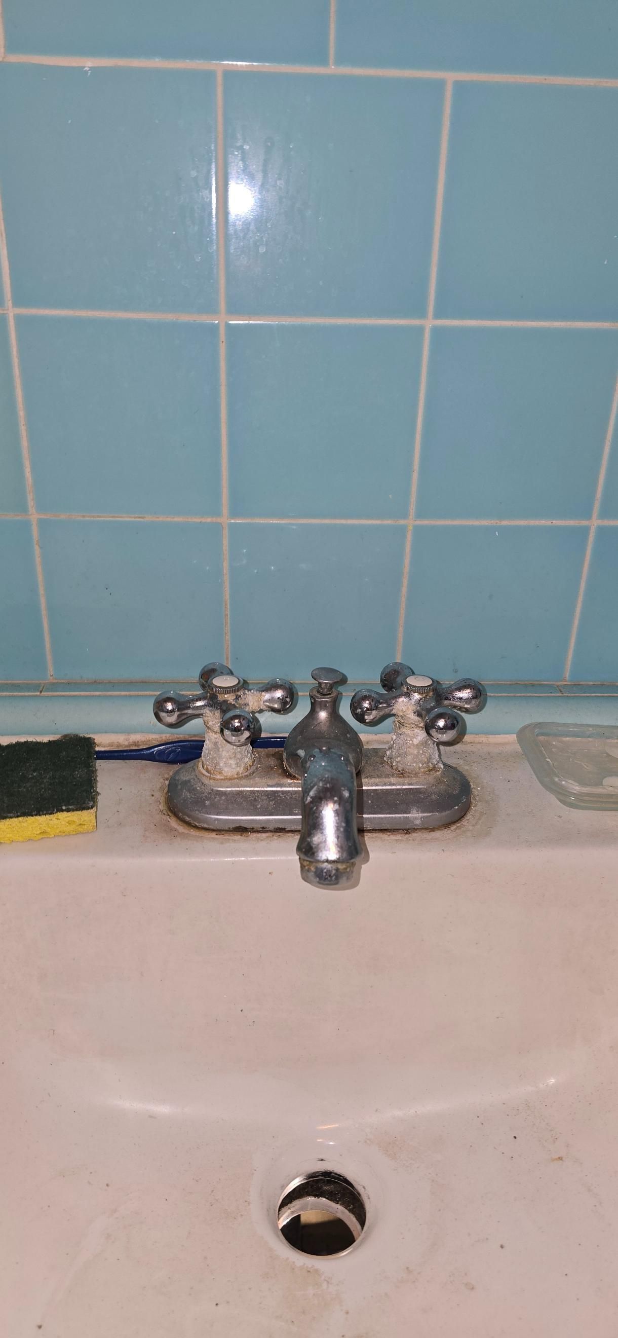Chrome sink faucet against blue tile bathroom wall over white basin.