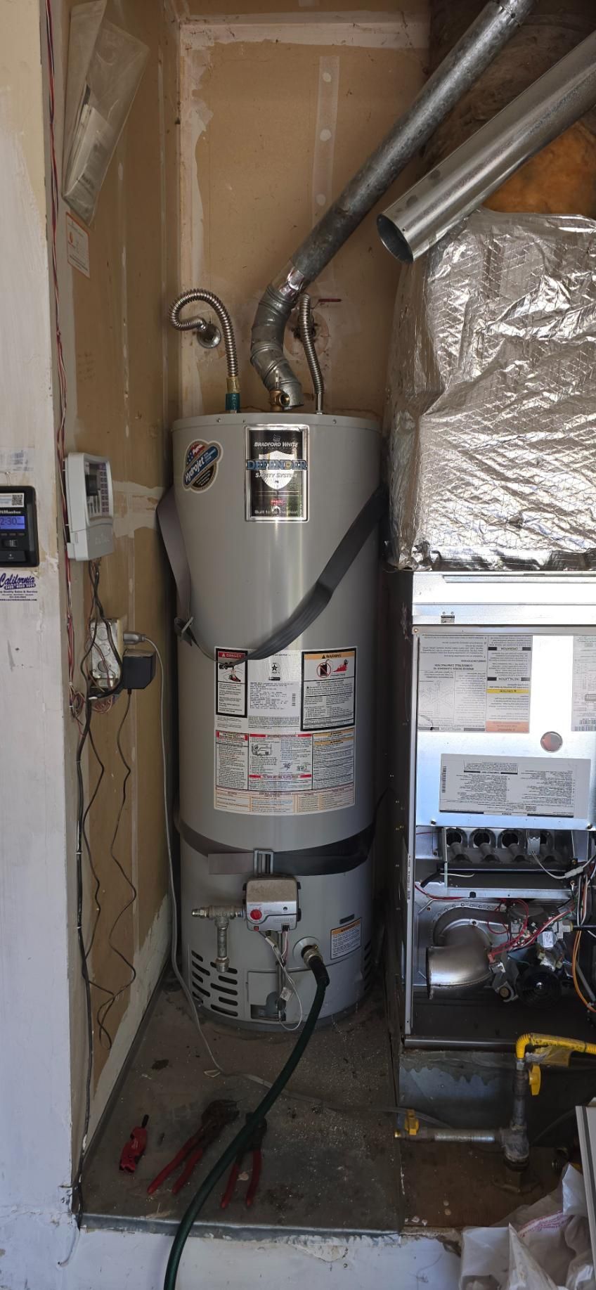 Water heater in a utility closet with exposed pipes, ductwork, and electrical components.