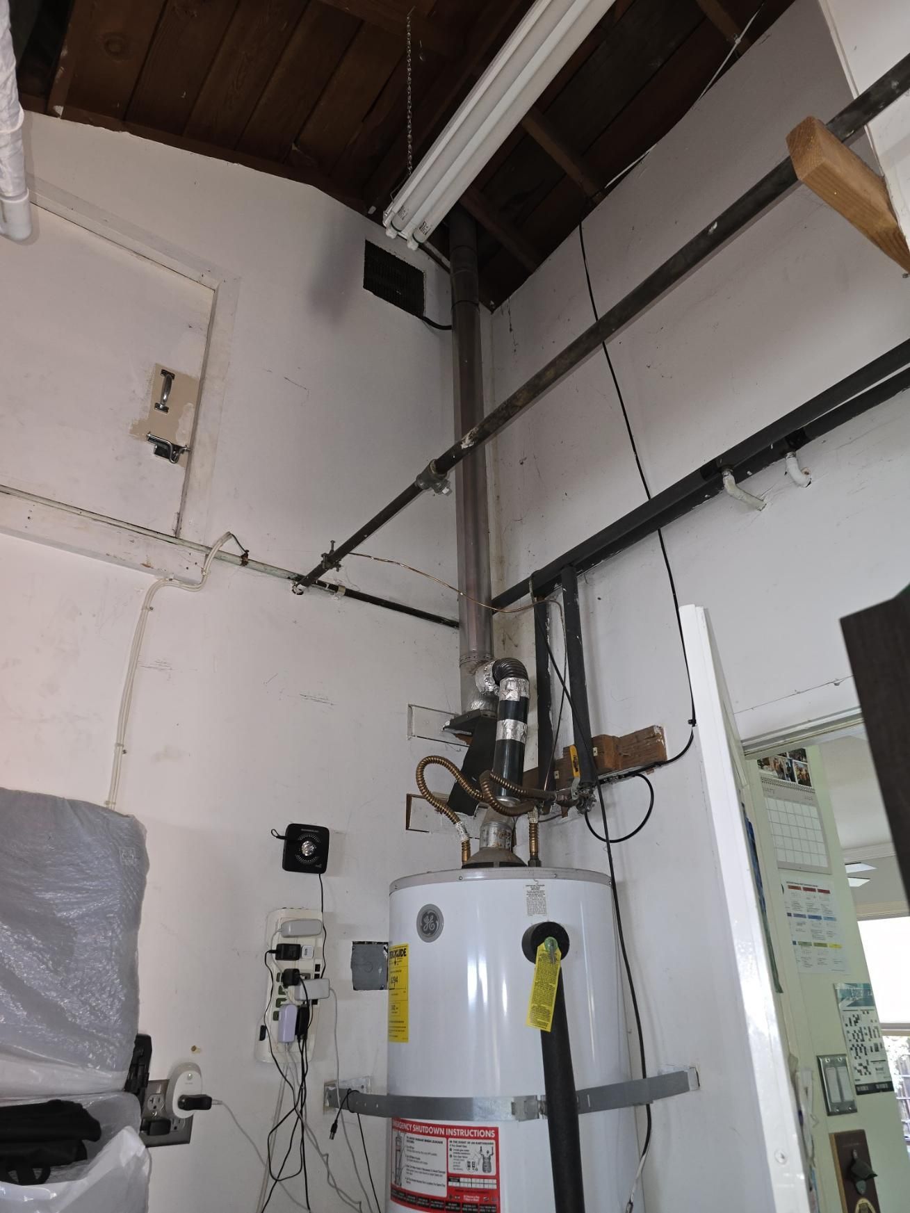 Utility room with water heater, exposed pipes, and electrical wiring on white walls