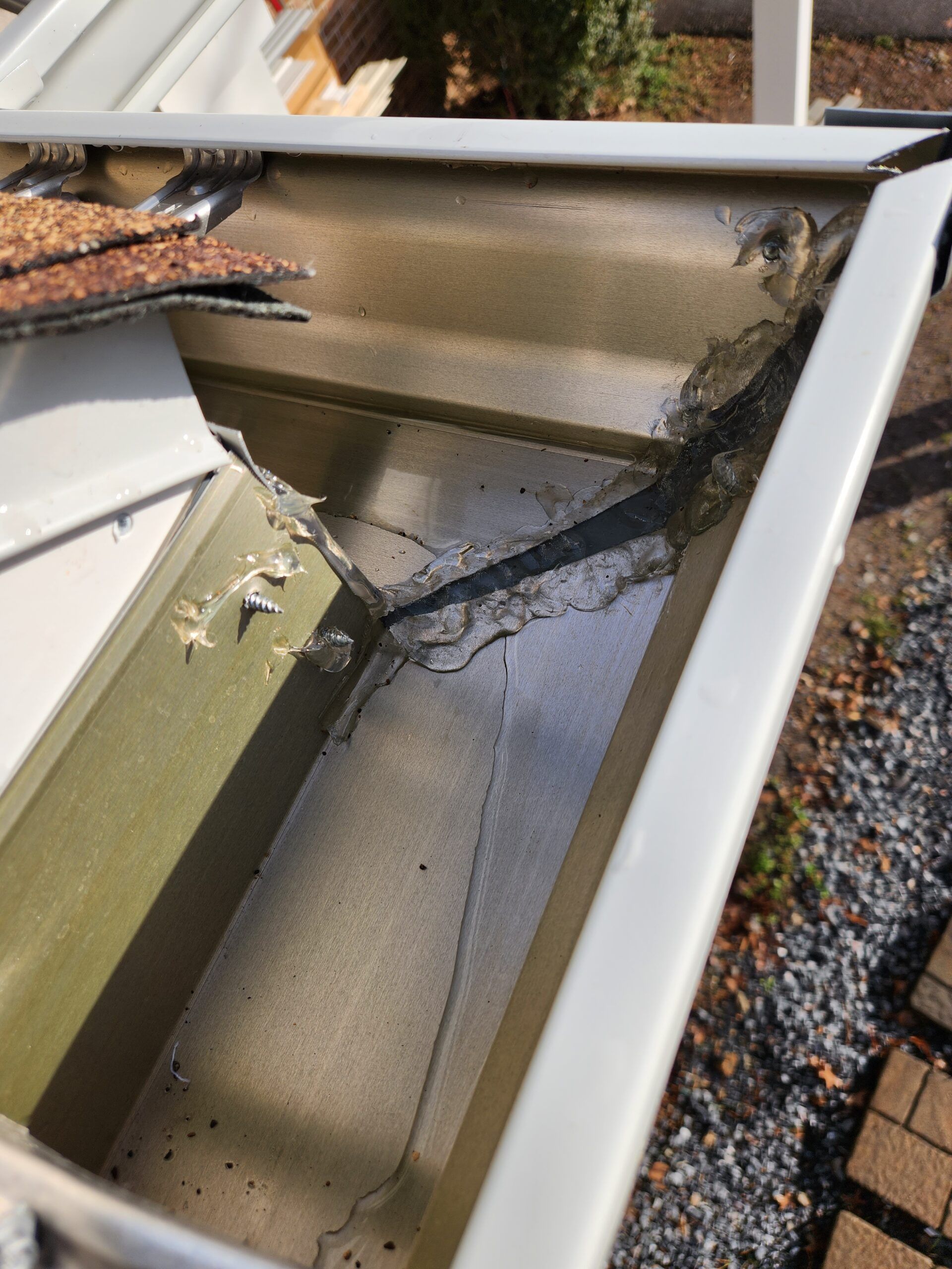 Close-up of a metal gutter corner joint sealed with dark, dried adhesive and showing signs of wear and gaps.