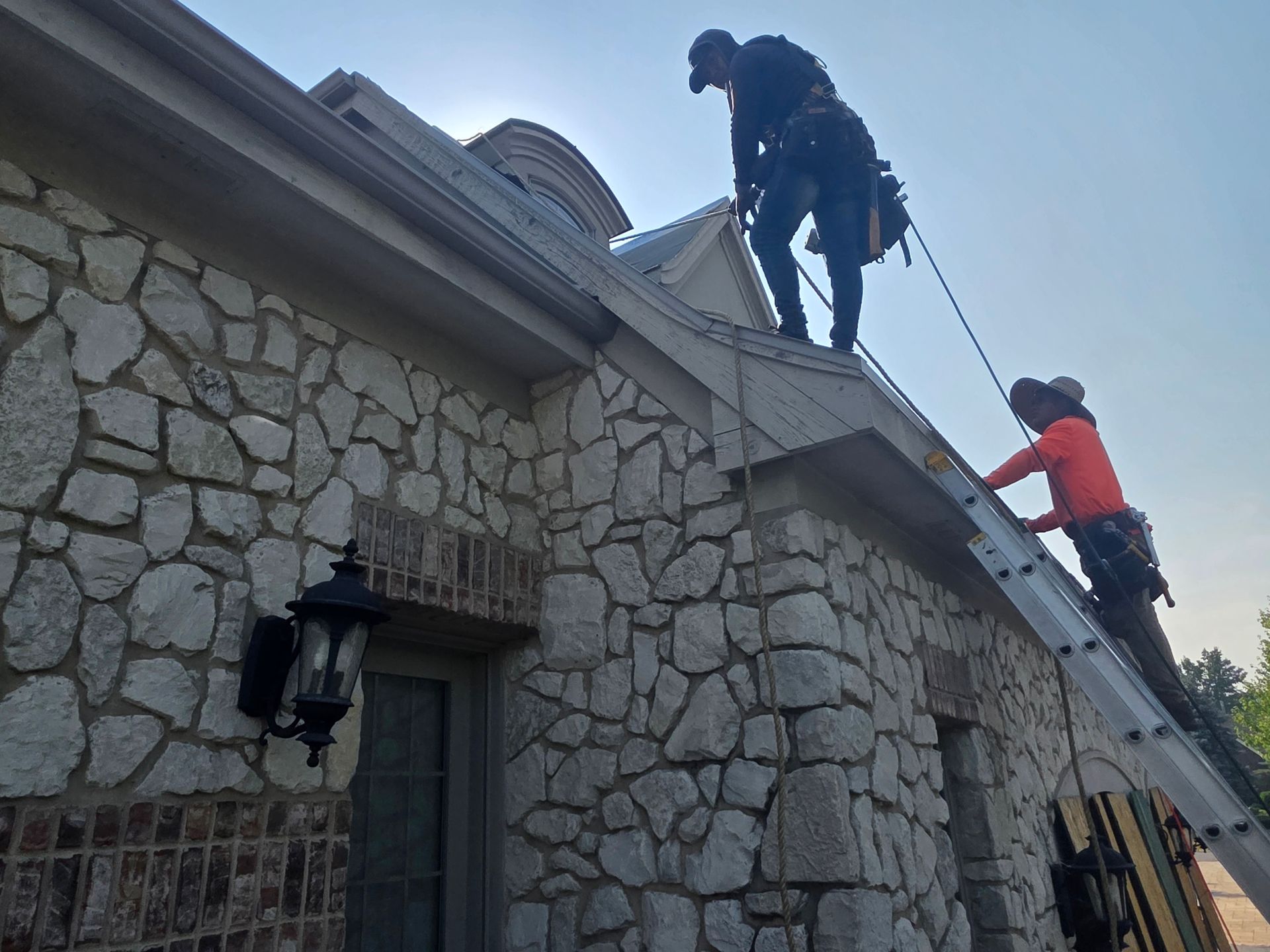 Four construction workers collaborate to repair the gutter and roof of a white building on a sunny day.