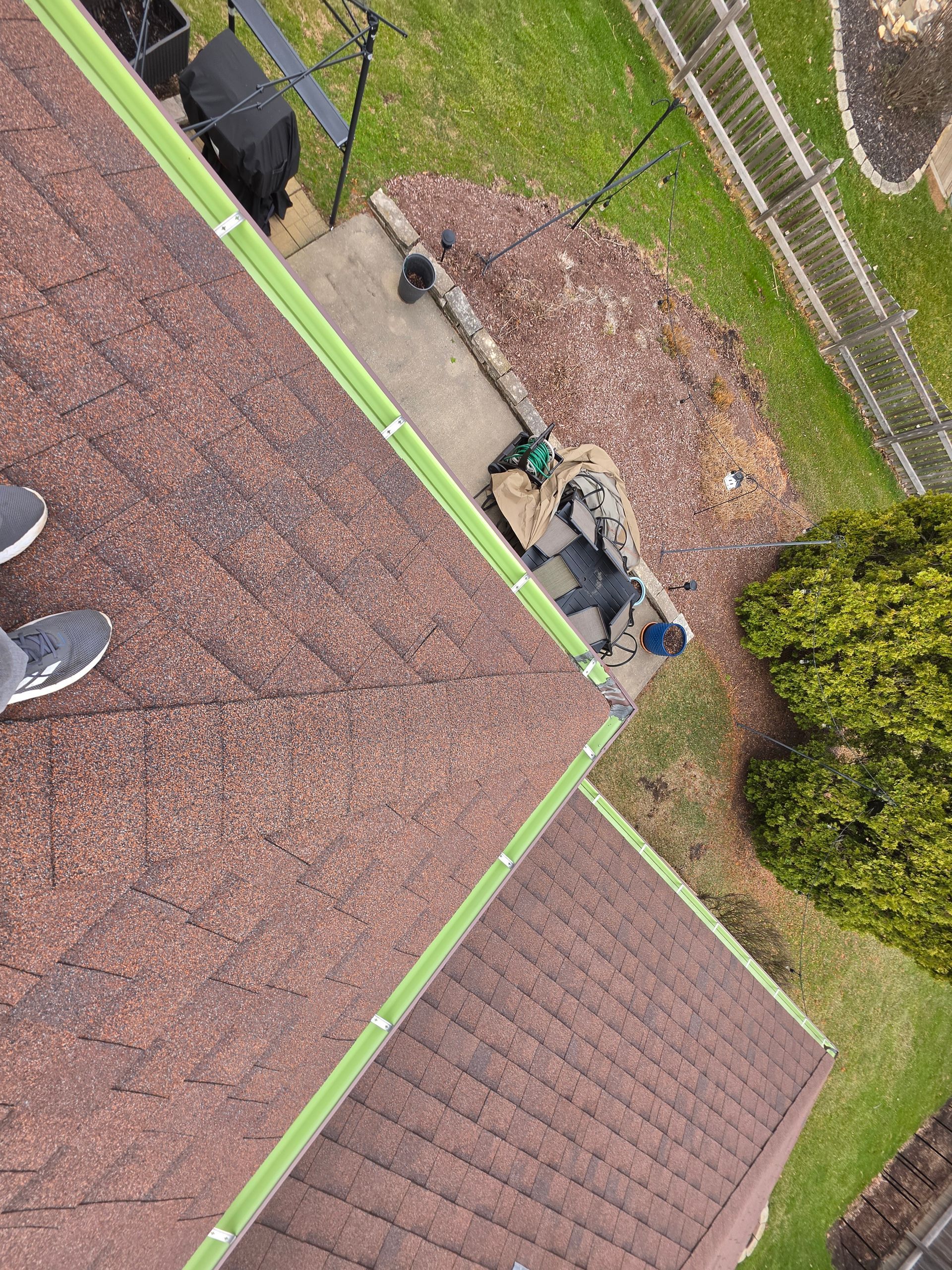 A first-person view looking down from a roof at a person working on the patio below, surrounded by mulch and grass.