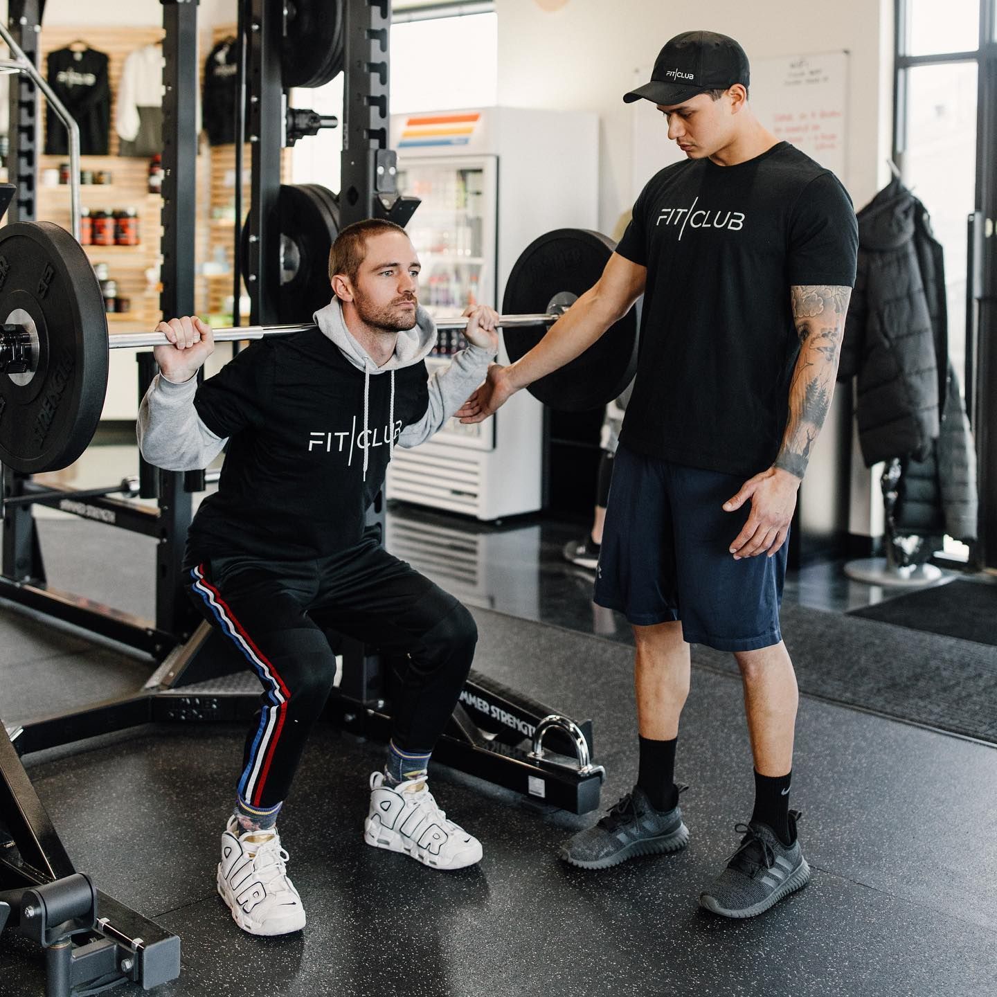 Personal training session at FitClub with barbell squat exercise for strength.