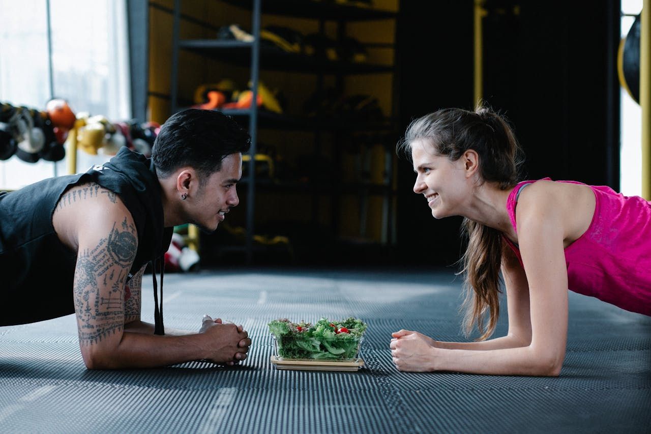 A man and a woman are doing plank exercises in a gym.