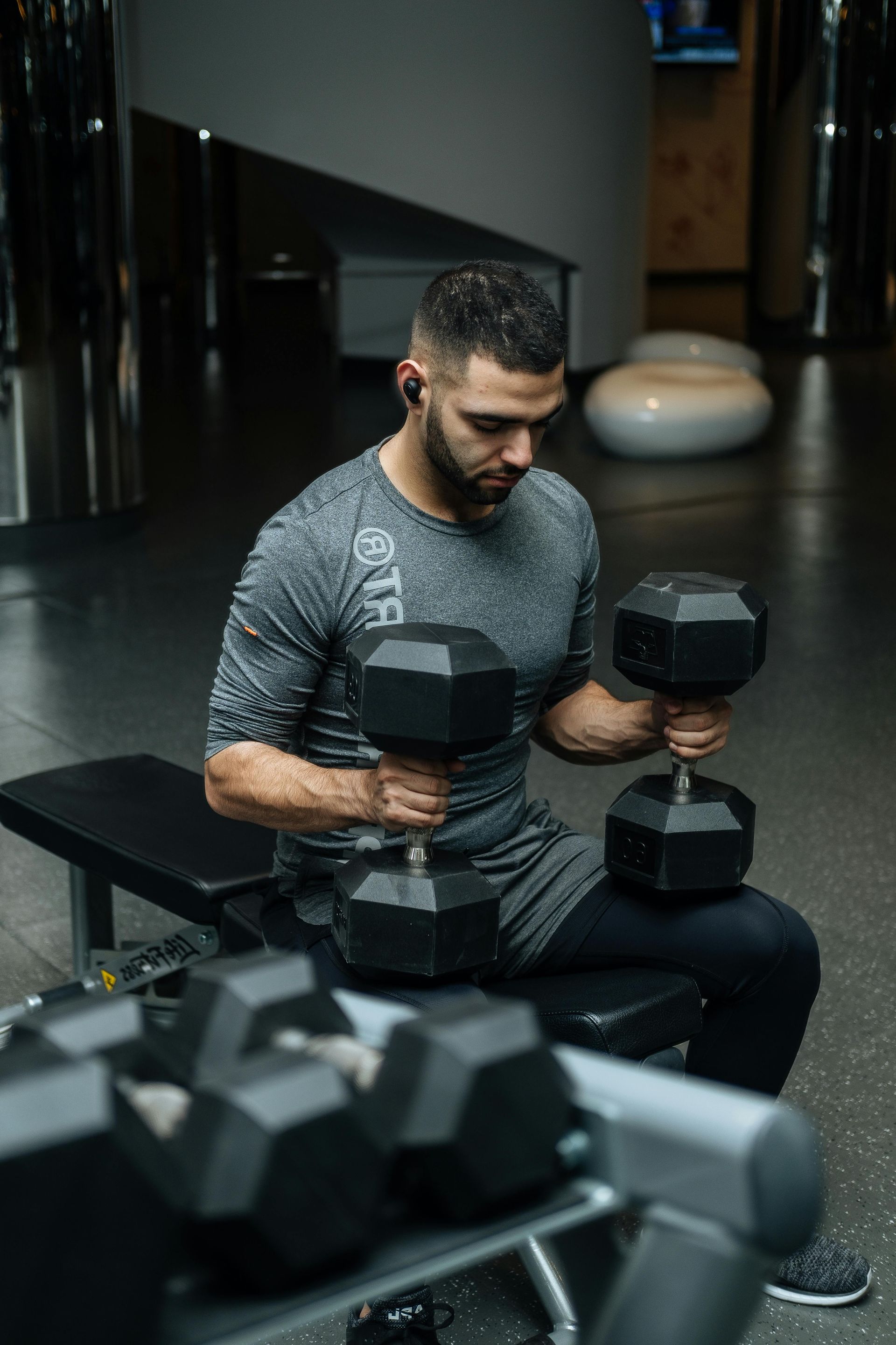 A man is sitting on a bench in a FitClub gym holding a dumbbell.