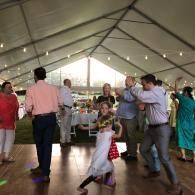 Guests dancing under a large white event tent, with a young girl in a white dress in the foreground.