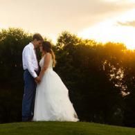 Bride and groom kissing at sunset on a grassy hill