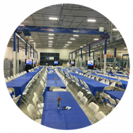 Large industrial banquet hall with long blue tablecloth-covered tables and rows of white folding chairs