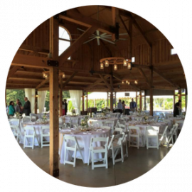 Rustic barn reception hall with round tables and white chairs set for an event