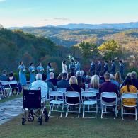 Outdoor wedding ceremony with guests seated on white chairs overlooking a mountain valley