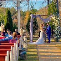 Wedding ceremony under a lavender arch in a garden, with bride and groom exchanging vows.