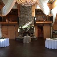 Elegant banquet hall with draped curtains, chandelier, stone fireplace, and round cocktail tables
