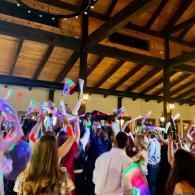 Crowd dancing indoors under wooden beams, waving colorful glow sticks at a lively event