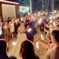 Outdoor wedding send-off with guests holding sparklers at night as the couple walks through an archway