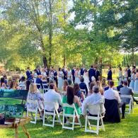 Outdoor wedding ceremony with guests seated on white chairs under trees in a park