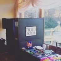 Promotional display table with black boards and a sign, set by bright windows with draped curtains.