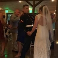Bride and groom dancing at a reception, with guests nearby and warm string lights overhead