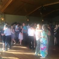 People dancing at a dimly lit indoor party, with sunlight streaming across the wooden floor.