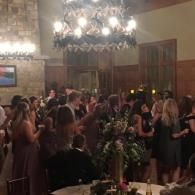 Crowded indoor party with people mingling under a chandelier and warm lighting
