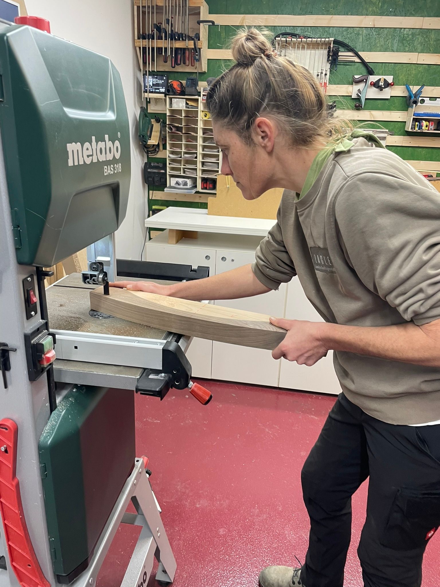 Eine Frau schneidet mit einer Metabo-Bandsäge ein Stück Holz