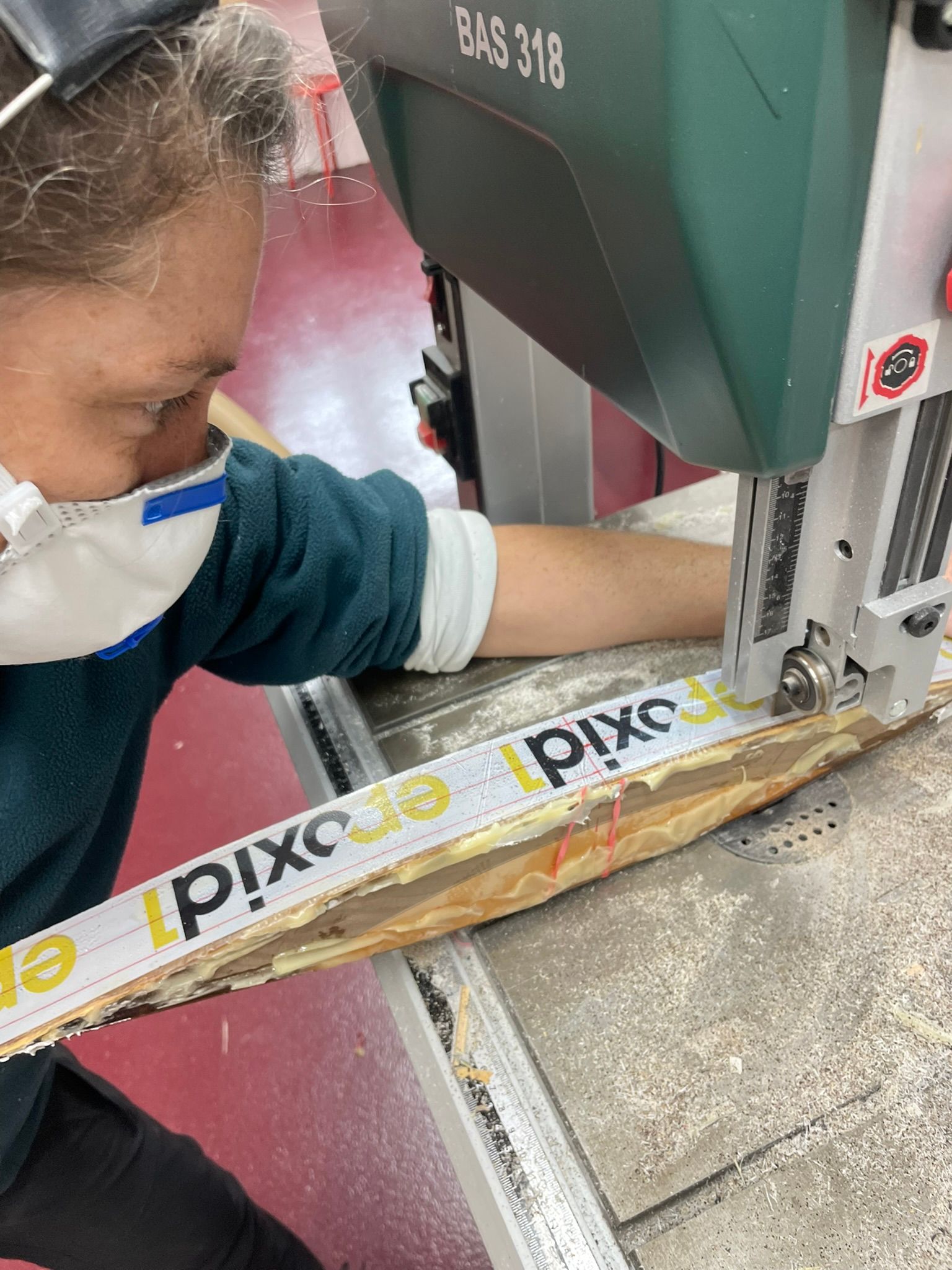 Eine Frau mit einer Maske schneidet mit einer Bandsäge ein Stück Holz