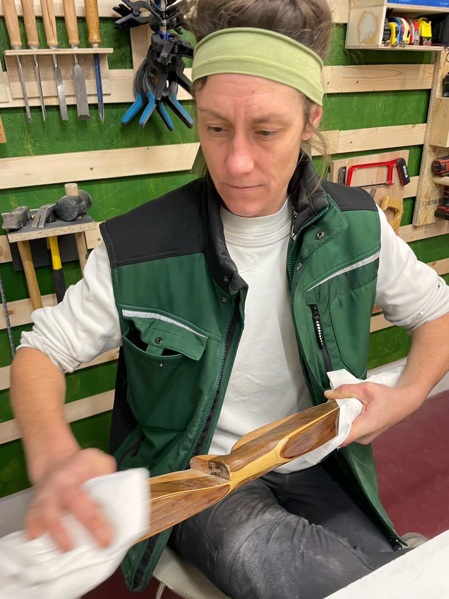 Eine Frau in einer grünen Weste putzt ein Stück Holz