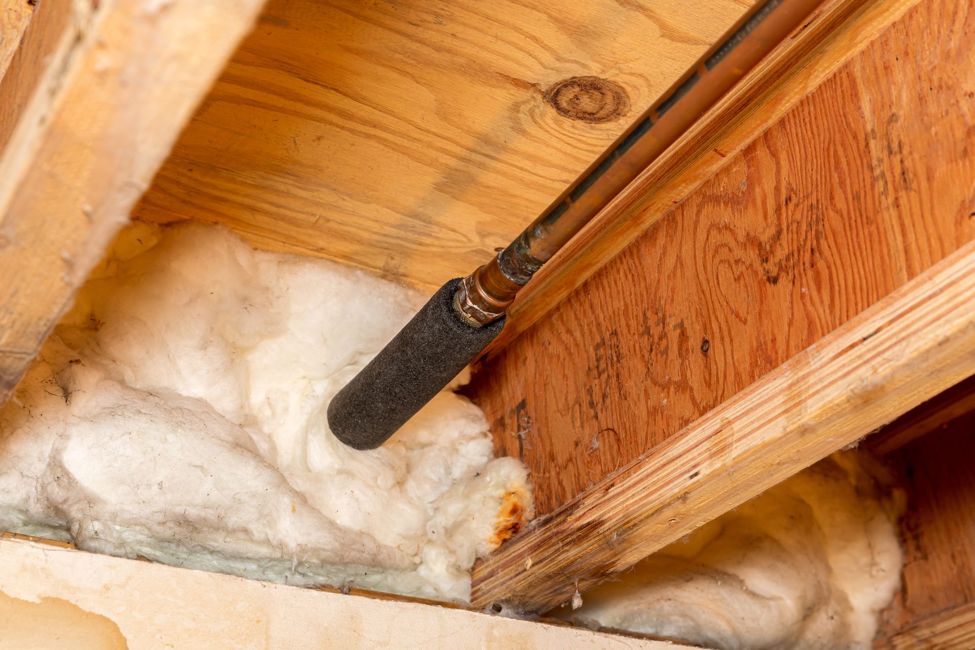 Insulated attic rafters with a black pipe running through white foam insulation